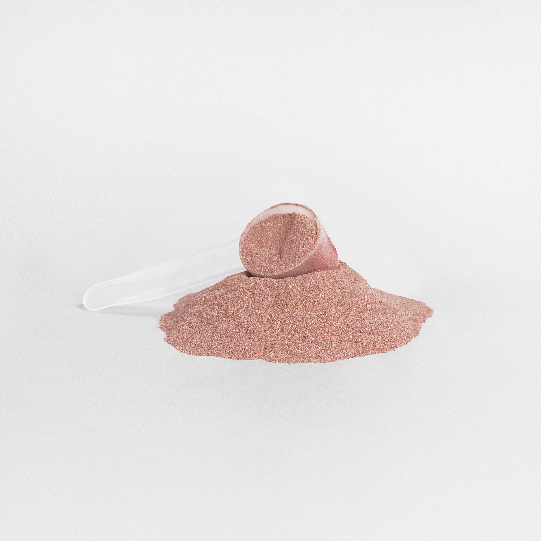 An Assure Reds Superfood Powder scoop from Habitly, filled with fine, reddish-brown powder rich in antioxidants, is tipped over, spilling its contents onto a white surface.