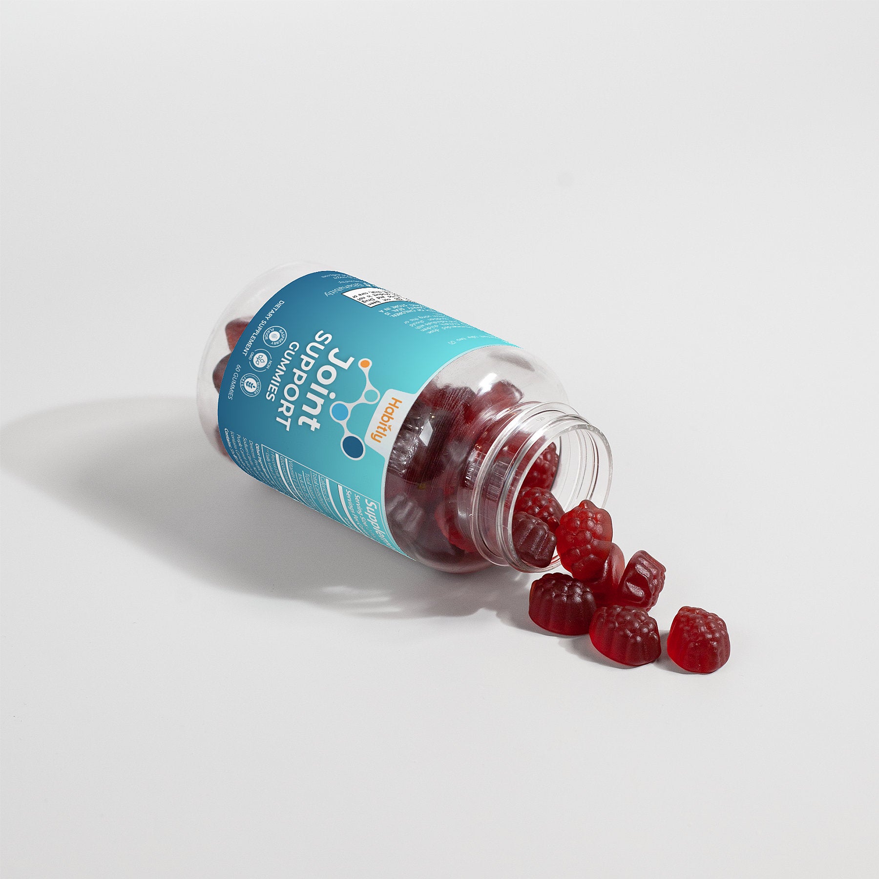 A tipped-over bottle of red gummy supplements on a white surface spills its contents, showcasing the label &quot;Joint Support Gummies (Adult)&quot; by Habitly. These glucosamine-infused gummies are scattered invitingly in front of the open container to promote joint health.