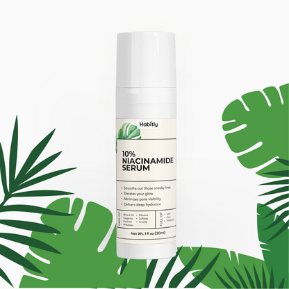 A Habitly 10% Niacinamide Serum bottle is centered against a white background with green tropical leaves. The white label highlights benefits such as smoothing lines, enhancing glow, minimizing pores, and providing hydration. Infused with Chamomilla Recutita Flower Extract, the bottle contains 1.1 fl oz (30 ml).