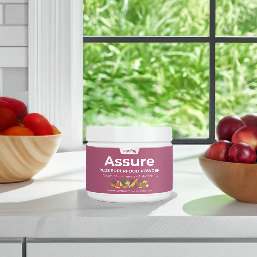 A container of &quot;Assure Reds Superfood Powder&quot; by Habitly, an effective dietary supplement abundant in antioxidants, is placed on a white countertop with bowls of fruit. A window in the background reveals a lush green garden.